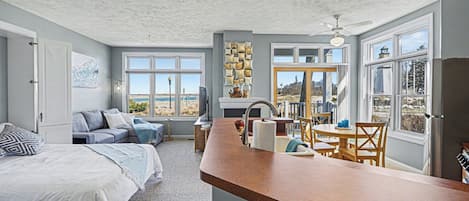 A compact living space with a kitchenette, a dining area, and a bedroom with a large window.