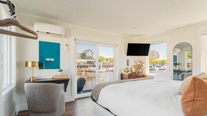 Habitación de hotel con una cama grande, un escritorio con lámpara, televisión y vista al puerto deportivo.