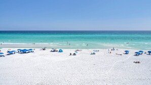 Een strand met wit zand, helderblauw water en blauwe parasols.