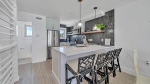 Een moderne keuken met een centraal eiland, roestvrijstalen apparatuur en een eethoek met zwarte stoelen.