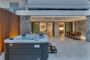 A modern outdoor hot tub area with a wooden fence, stone walls, and a dining table with chairs.