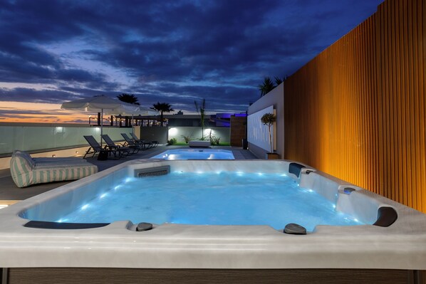 Un espace piscine aménagé sur le toit, avec des bains à remous, des chaises longues et un mur en bois.