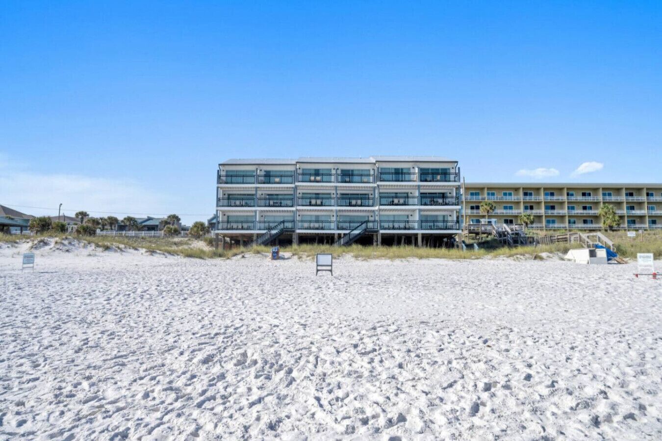 A beachfront hotel with multiple balconies, a sandy beach in front, and a clear sky.