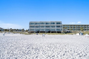 Een hotel aan het strand met meerdere balkons, een zandstrand ervoor en een heldere lucht.