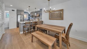A modern kitchen with a central island, wooden dining table, and chairs. - Beachfront | Top-Rated | Sleeps 10 | Seabatical #3 (Destin)
