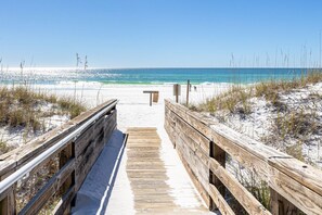 A wooden boardwalk leading to a beach with a bench and a sign. - Violet Sands Gulf Front 2 Bedroom with Multiple Pools (Miramar Beach)