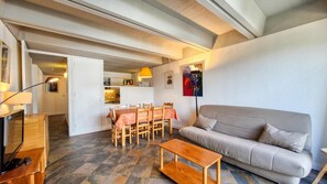 Ein Wohnzimmer mit einer Couch, einem Holztisch, einem Fernseher und einem Essbereich mit Tisch und Stühlen.