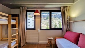Ein Zimmer mit Etagenbetten, einer roten Hängelampe, einem kleinen Hocker und einem Bett mit roten Kissen.