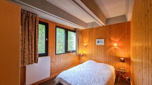 Ein Zimmer mit Holzwänden, einem Bett, zwei Fenstern und zwei Wandleuchten.