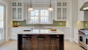 A modern kitchen with white cabinetry, a central island with stools, stainless steel appliances, and pendant lighting. - EAST HAMPTON VILLAGE JEWEL BOX (East Hampton)