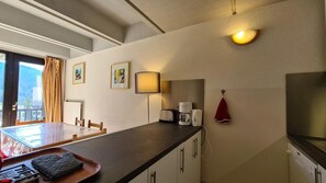 Eine kompakte Küche mit Essbereich, einer Kaffeemaschine, einer Lampe und einem roten Handtuch an der Wand.