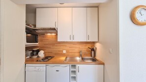 Eine kleine Küche mit weißen Schränken, einer Holz Arbeitsplatte, einem Geschirrspüler von Bosch, einem Spülbecken und einer Uhr an der Wand.