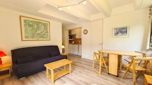 Ein Wohnzimmer mit einer Couch, einem Holztisch und einer Küche im Hintergrund.