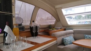 Interior de un yate con zona de comedor, panel de control y sala de estar con cojines.