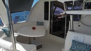 Interior de un barco con una pequeña mesa, dos zonas de asiento acolchadas y un panel de control.