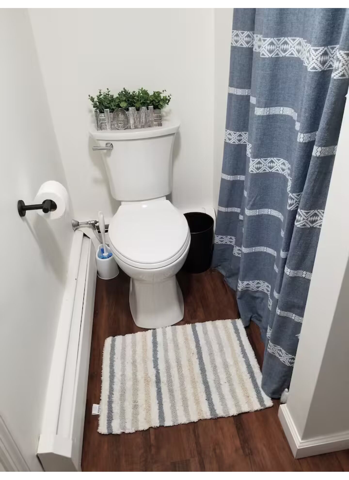 Ein Badezimmer mit Toilette, einem kleinen Mülleimer, einem weißen Heizkörper, einem Streifen Teppich und einem blauen, gemusterten Duschvorhang.