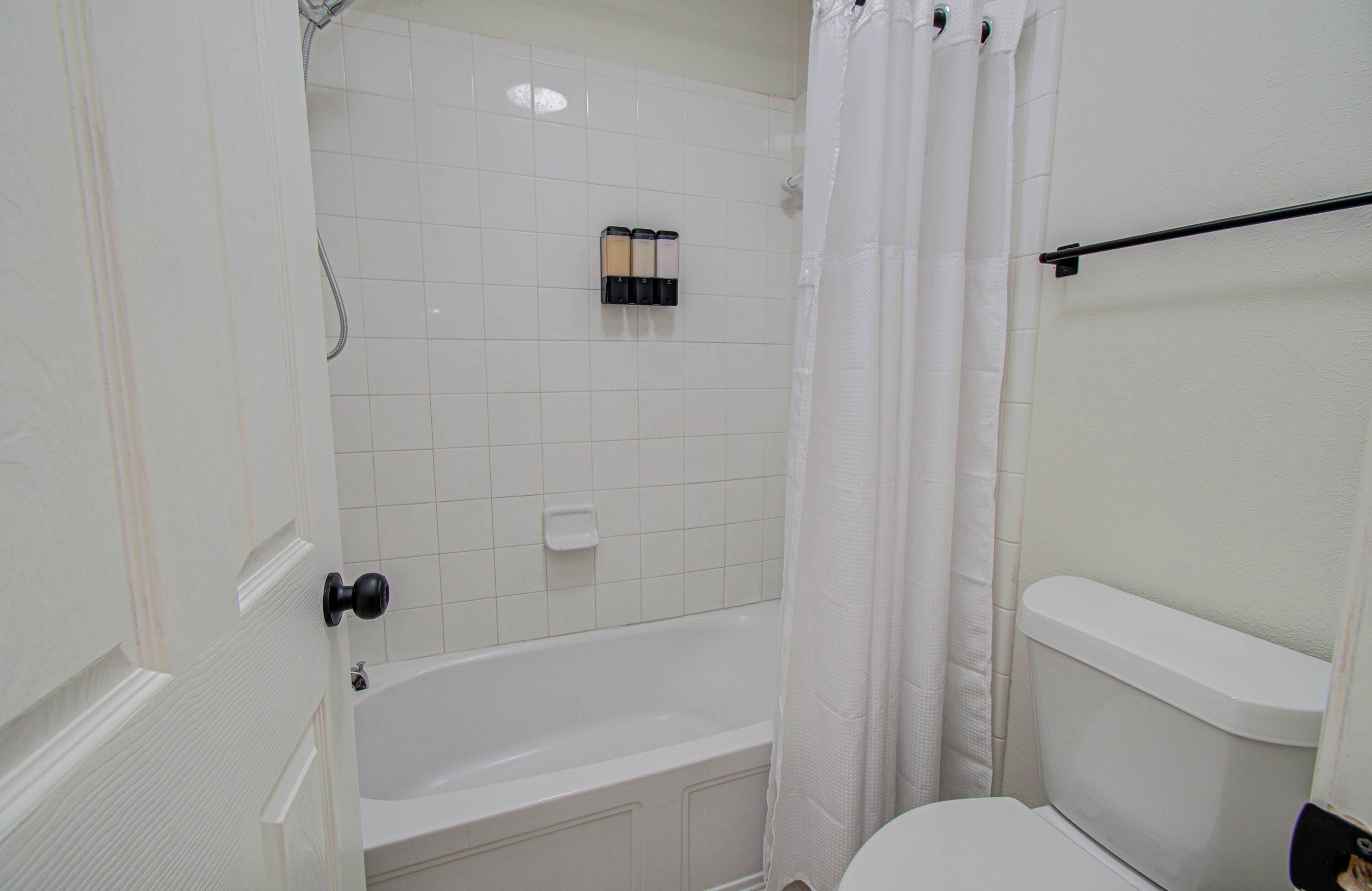 A bathroom with a bathtub, toilet, and shower curtain.