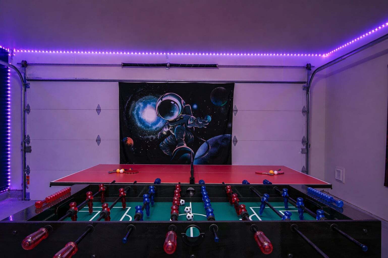 A room with a foosball table, a space-themed painting, and purple LED lights.