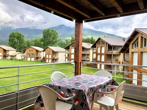 Ein überdachter Außenbereich mit Tisch und Stühlen, mit Blick auf eine gebirgige Landschaft und mehrere Holzhäuser.
