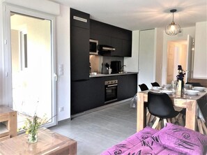 Eine moderne Küche mit schwarzen Schränken, einem Einbauofen und einem Essbereich mit Holztisch und -stühlen.
