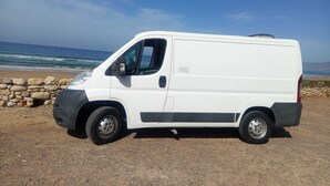 Una camioneta blanca estacionada en una playa rocosa con el océano al fondo.