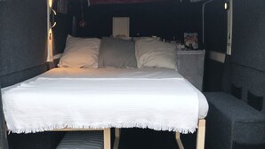 Interior de una furgoneta con una cama, una mesita y una silla.