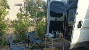 Una caravana con interior cubierto, dos sillas plegables, una pequeña mesa con objetos y suelo de grava.