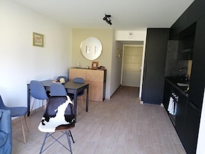 A modern kitchen with black cabinets, a dining area with a round mirror, and a light-colored tiled floor. - 300m from shops, Ground floor, parking, tv, ski locker, 49m², Pra Loup (Barcelonnette)