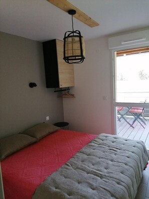 A bedroom with a bed, a hanging light fixture, a wardrobe, a small table, and a view of the outside. - 300m from shops, Ground floor, parking, tv, ski locker, 49m², Pra Loup (Barcelonnette)