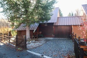 Ein rustikales Blockhaus mit einem Kiesweg, der zu einer Holztür führt, umgeben von einem Schotterhof und einem Holzzaun.