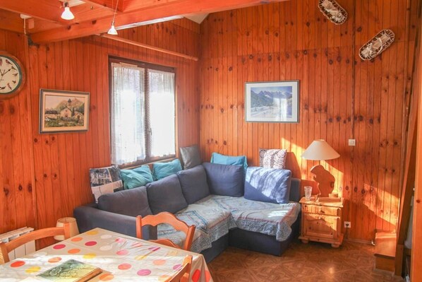 Ein gemütliches Blockhaus-Interieur mit Holzausstattung, einer Couch, einem Esstisch und einer Lampe.