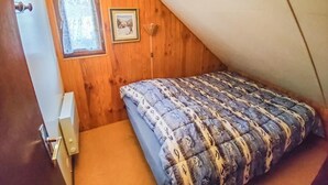 Un petit i acollidor dormitori al menjador, amb un sostre inclinat, un llit individual, una finestra amb cortina i un quadre al mur.