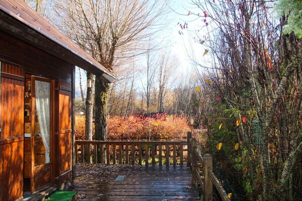 Eine Holzhütte mit Veranda, einer Holzterrasse und Blick auf Herbstlaub.