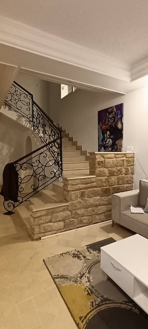 Un escalier avec des rampes en métal ouvragé, un mur en pierre, un tableau, un canapé et une table blanche.