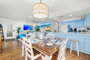 A modern kitchen with blue cabinets, a dining area with a wooden table and white chairs, and a ceiling fan. - Gulf View • 199 Steps to Beach • Dog-Friendly (Indian Rocks Beach)