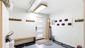 Ein Zimmer mit einer Bank, einer Tür, einem Wandregal, einer Matte und einer Wand mit Haken.