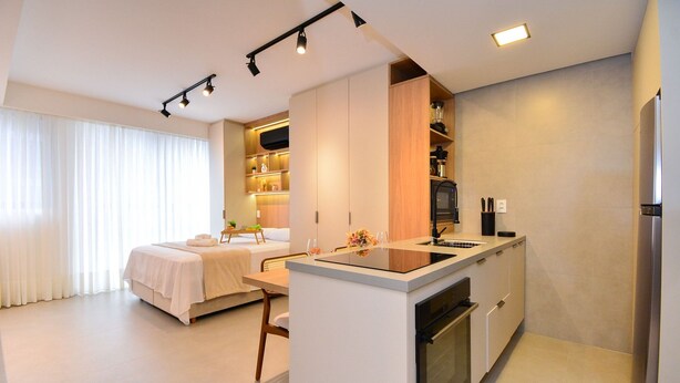A modern kitchen with a central island, built-in appliances, and a dining area with a sofa and table. - Elegante Studio frente a UFSC e HU -201R (Florianópolis)