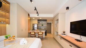 A modern hotel room with a bed, a small kitchenette, a dining area, and a TV. - Elegante Studio frente a UFSC e HU -201R (Florianópolis)