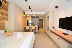 Ein modernes Hotelzimmer mit einem Bett, einer kleinen Küchenzeile, einem Essbereich und einem Fernseher.