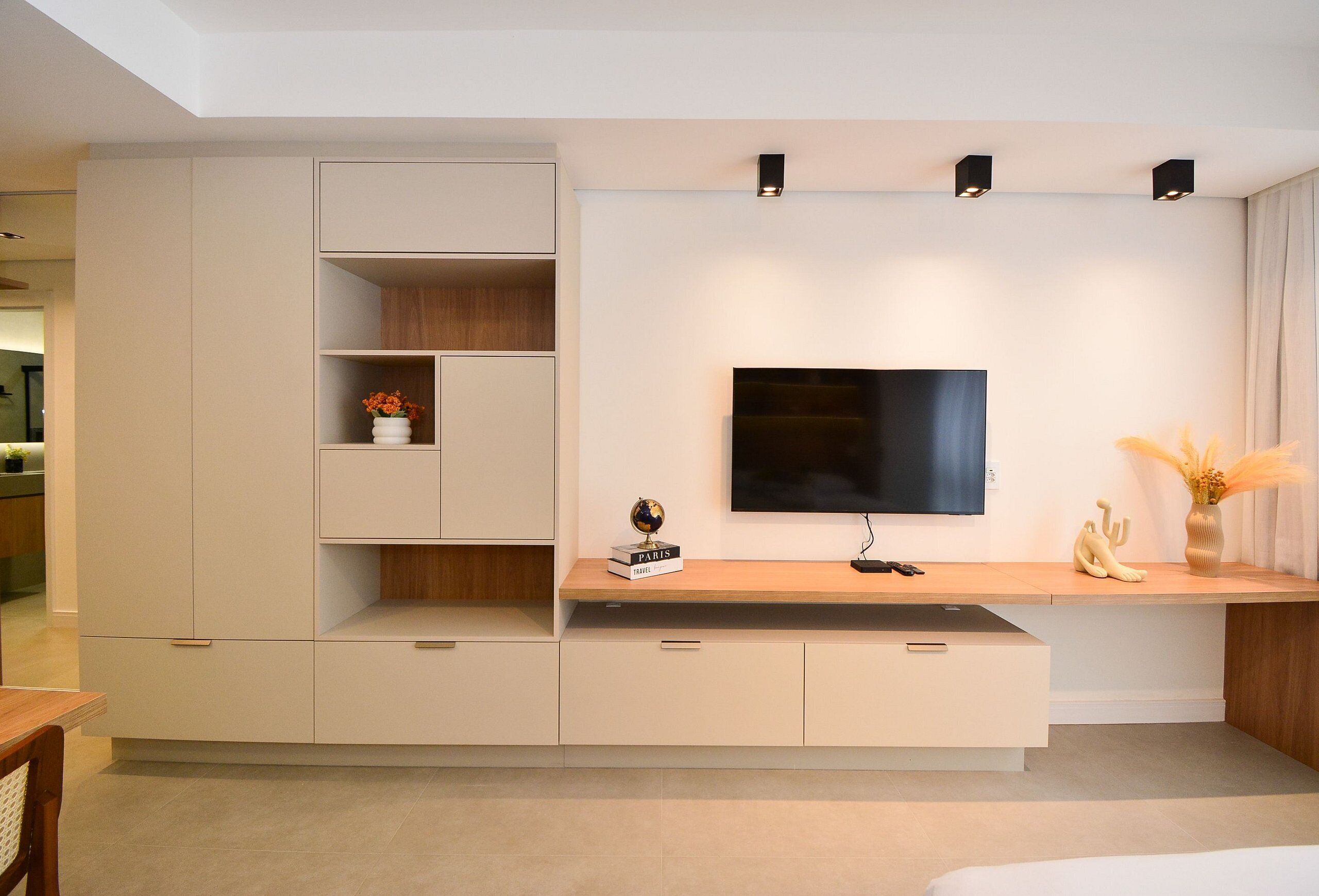 Een moderne woonkamer met een flatscreen televisie aan de wand, een houten salontafel en inbouwkasten.