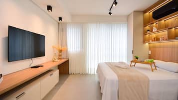Una habitación de hotel moderna con televisor de pantalla plana, una mesita consola de madera, una cama con colcha blanca y una mesita de noche con bandeja.
