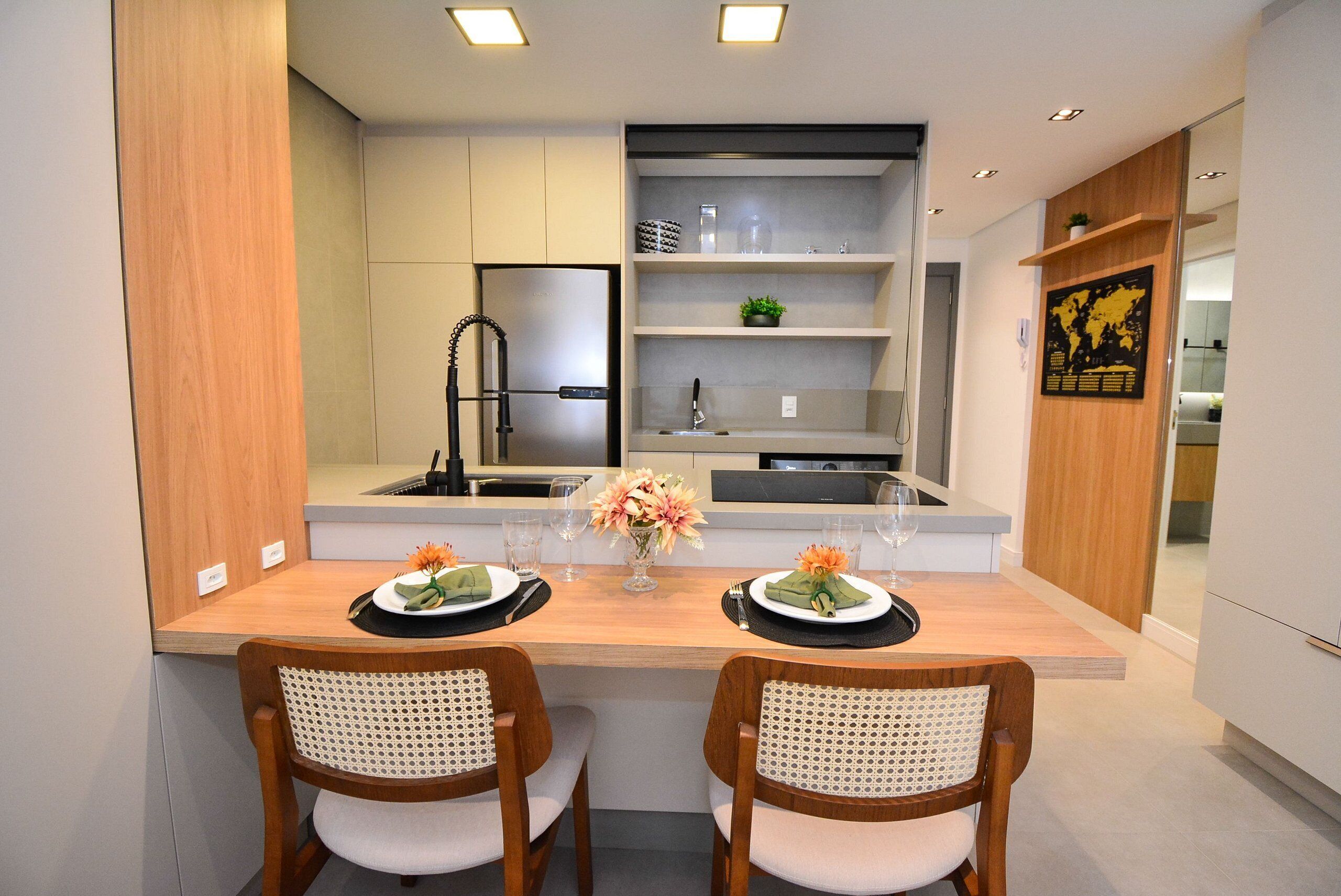 Une cuisine moderne dotée d’un îlot central, de deux chaises, d’un réfrigérateur et d’une étagère où sont disposés des objets décoratifs.