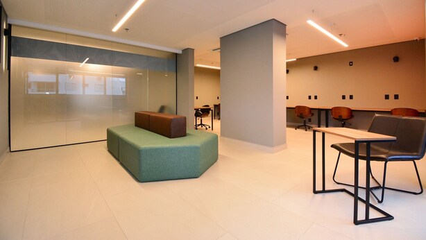 A modern office space with a glass partition, a green cushioned seating area, and a table with chairs. - Elegante Studio frente a UFSC e HU -201R (Florianópolis)