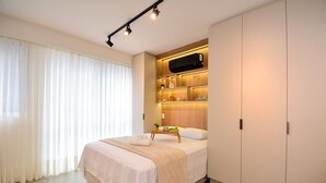 A modern bedroom with a bed, bedside tables, a wardrobe, and a built-in shelf with decorative items. - Elegante Studio frente a UFSC e HU -201R (Florianópolis)
