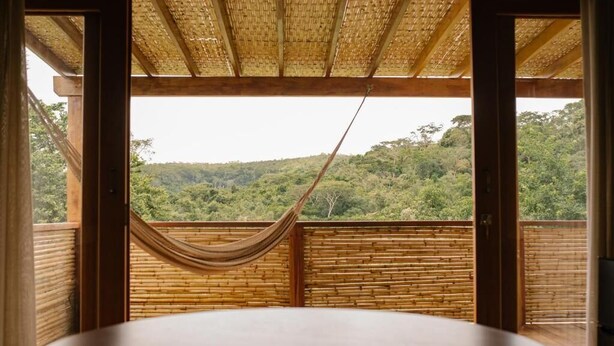 A room with a large window, a hammock, and a view of a forested hill. - Canto dos Pireneus Hospedaria (Pirenopolis)