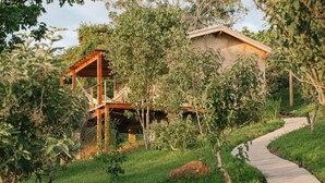 A rustic wooden structure with a staircase leading up to a house, surrounded by lush greenery and a winding path. - Canto dos Pireneus Hospedaria (Pirenopolis)