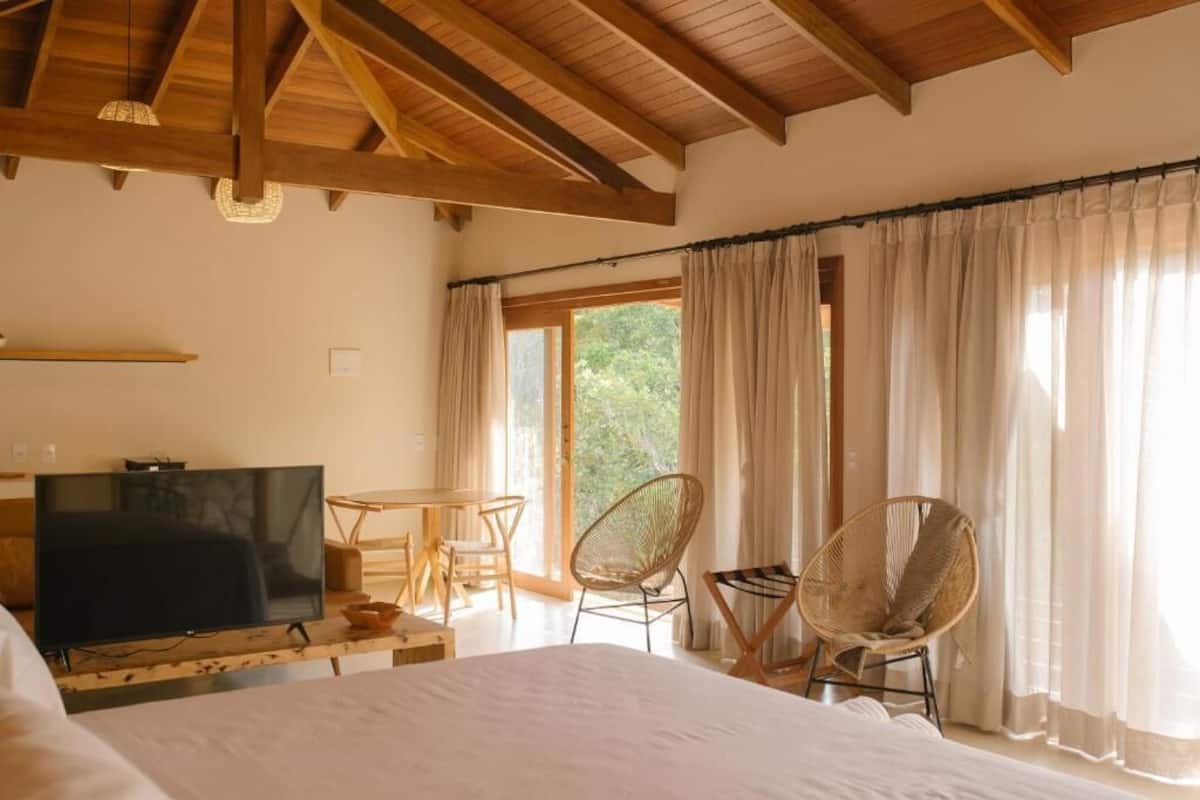 A bedroom with a bed, a TV, a dining table, and two chairs.