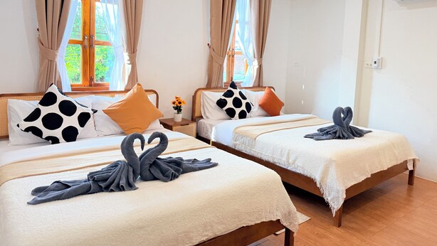 Zwei Betten mit in Schwanform drapierten Handtüchern, beige Vorhänge und ein Fenster mit Blick ins Grüne.