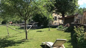 Un patio trasero con césped, una silla de jardín, una cerca de madera y un edificio de piedra al fondo.