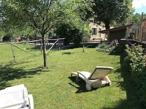 A grassy backyard with a lawn chair, a wooden fence, and a stone building in the background. - Comfortable gîte in a peaceful mountain setting (Graye-et-Charnay)